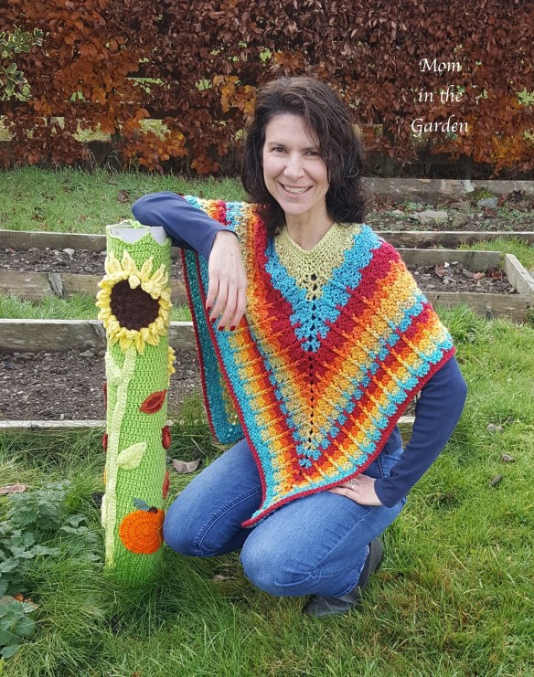 mom in the garden kneeling at flowerbombed pipe in the garden wearing rainbow poncho