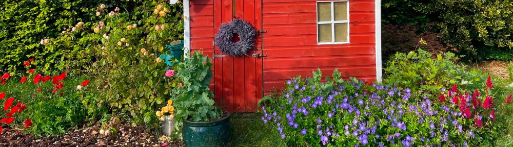 Red playhouse with lavender wreath on front door and purple geranium.